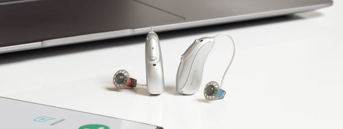 A pair of silver Phonak Lumity L90 hearing aids on a table.