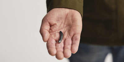 person holding black signia styletto AX hearing aid on palm