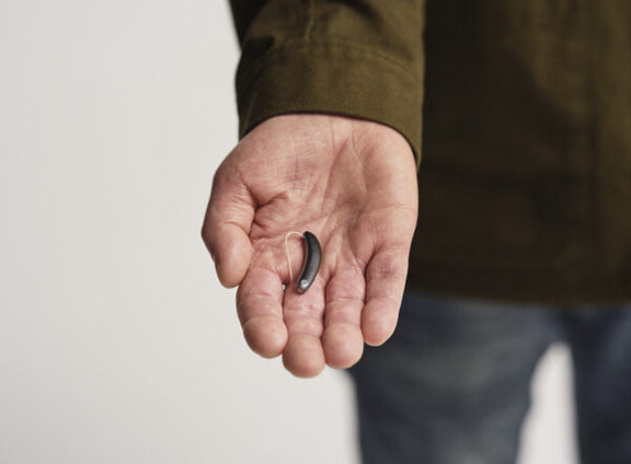 person holding black signia styletto AX hearing aid on palm