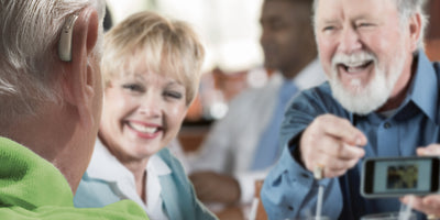 Older people out for dinner laughing and chatting at table wearing a Phonak hearing aid.