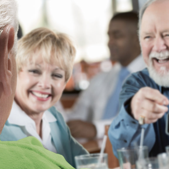 Older people out for dinner laughing and chatting at table wearing a Phonak hearing aid.