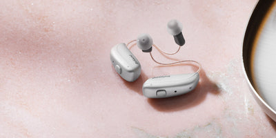 A pair of Resound Nexia 9 RIC silver hearing aids on a table.