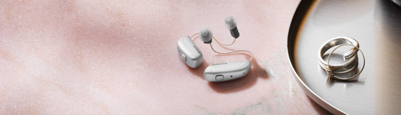 A pair of Resound Nexia 9 RIC silver hearing aids on a table.